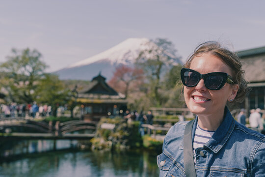 Woman wearing sunglasses poses with at Oshino Hakkai traditional thatched roof village near Mt Fuji, Japan