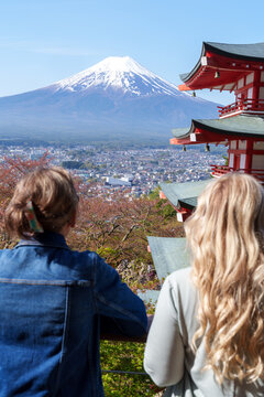 Intentionally defocused two women travelers pose at Chureito pagoda, Mt Fuji mountain viewpoint in Shimoyoshida, Japan. Enjoying view
