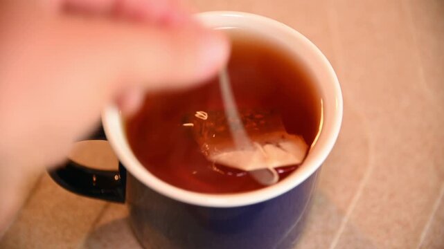 Tea bag being dipped and removed in ceramic mug on kitchen counter