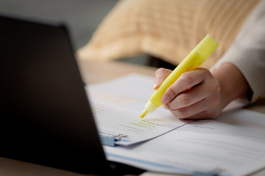 Exam preparation concept. Student highlighting important information while studying with printed documents and a laptop at home for online learning and test revision. Study, exam, highlight, learning,