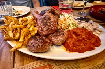 Fototapeta premium Enjoying mixed grill during a trip to Banskp, Bulgaria - a tasty mix of various grilled meats and vegetable based sauces and salads