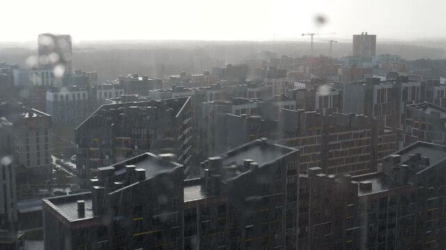 Heavy rain falling on modern apartment buildings in new residential district, with moody, overcast sky. Raindrops blurring view from window creating gloomy atmosphere