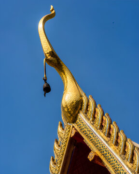 Golden Chofa and small bell detail on a traditional Thai Buddhist temple roof against a clear blue sky.