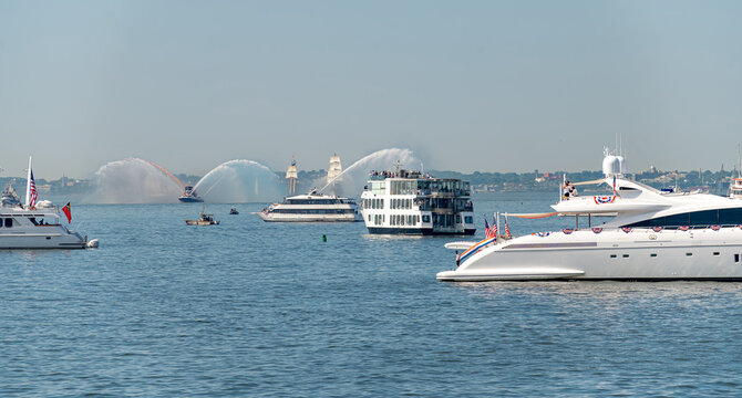 Boats and luxury yachts in New York Harbor. Fireboats spray large water fountains near white ships on a clear summer day.