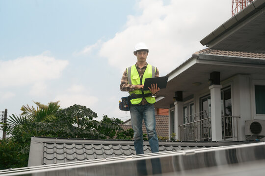 Solar Panel Technician Inspecting Rooftop Installation on Residential Home with Laptop