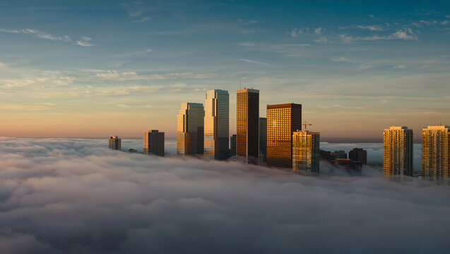 Cityscape sunrise breaking through morning fog and clouds above urban skyline