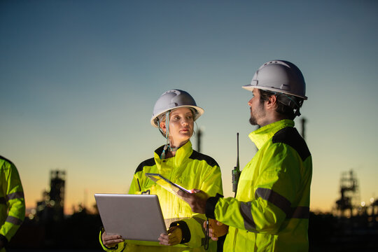 Engineers discussing construction plans at dusk with safety gear and equipment in industrial setting