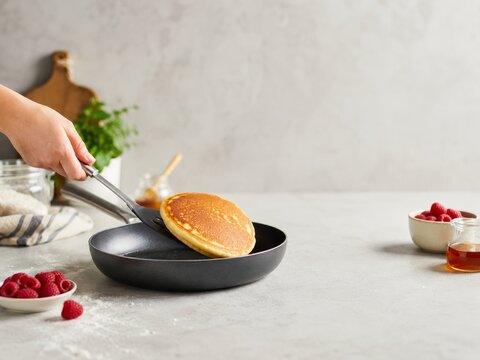 Cocinar pancakes en una sart&eacute;n con frutas en la mesa