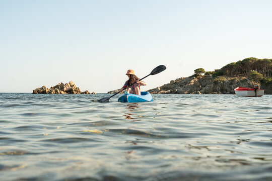 Kayaker paddling on calm sea near rocky coast at sunset