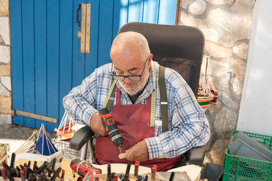 Elderly artisan crafting wooden model boat in Palamos