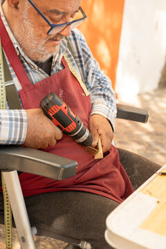 Elderly craftsman drilling wood in Palamos workshop scene