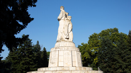 Obraz premium Monumental socialist-era stone statue in a public park under a clear blue skyLow-angle view of a monumental socialist-era stone statue standing in a public park on a sunny day. The imposing sculptur