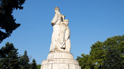Fototapeta premium Monumental socialist-era stone statue in a public park under a clear blue skyLow-angle view of a monumental socialist-era stone statue standing in a public park on a sunny day. The imposing sculptur