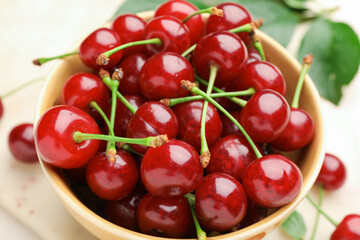 Obraz premium Fresh ripe cherries in bowl and green leaves on table, closeup
