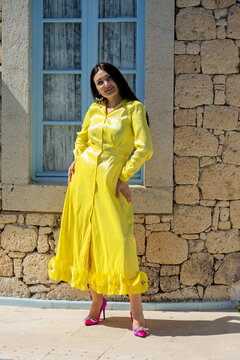 Woman in yellow dress posing outdoors by stone wall