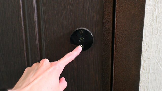 Human finger presses video doorbell button on dark wooden door