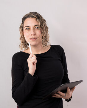 Thoughtful woman holding a digital tablet while raising one finger as if developing a new idea or solution. Professional studio portrait representing creative thinking, planning, problem solving, stra