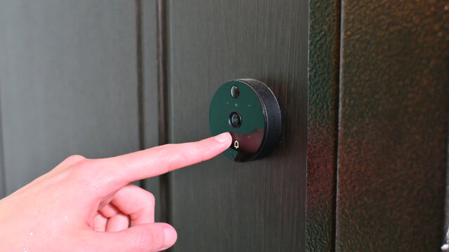 Human finger presses video doorbell button on dark wooden door