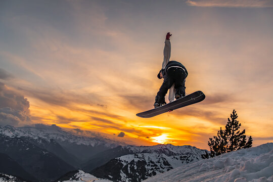 Snowboarder jumps at sunset in snowy mountains