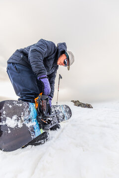 Snowboarder adjusting bindings on snowy slope