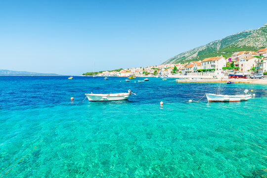 Traditional seaside houses and fishing boats along crystal clear Adriatic sea coast in Bol town on Brac Island, Croatia. Mediterranean travel, coastal living, island vacations, waterfront tourism