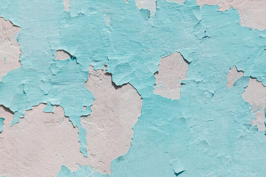 Peeling turquoise paint reveals faded white plaster beneath