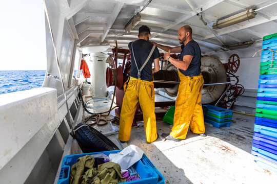 Fishermen working on trawler deck with net winch at sea