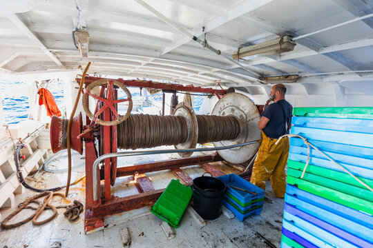 Fisherman operating winch on trawler deck at sea