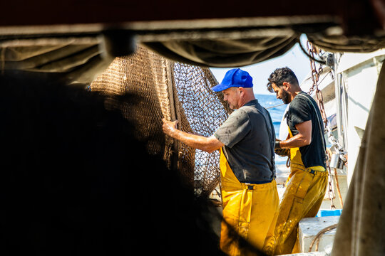 Fishermen hauling trawl net on working boat at sea