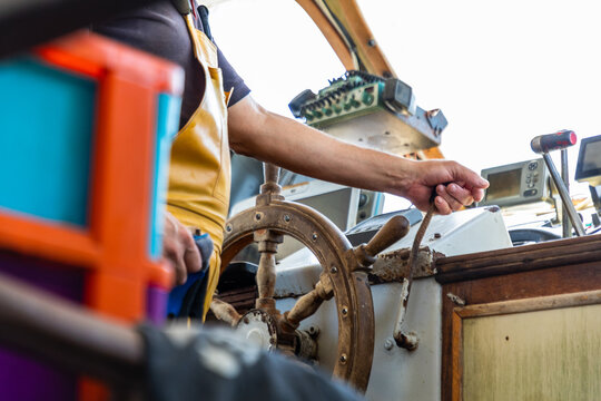 Fisherman steering boat at helm with wooden wheel and throttle