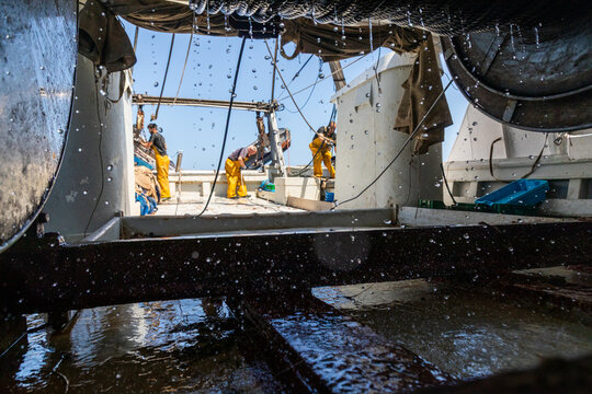 Fishing crew at work on trawler deck with sea spray