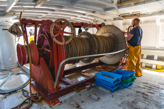 Crewman monitoring trawl winch and steel cable on deck
