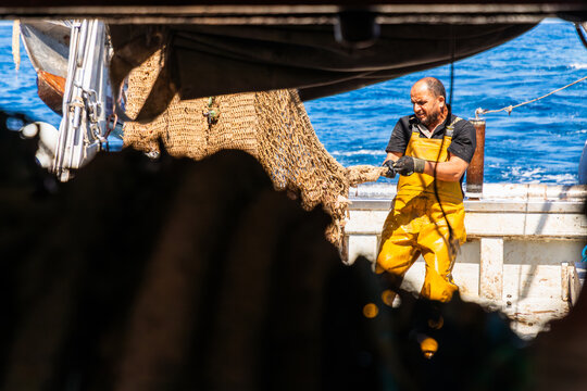 Fisherman hauling trawl net on working boat at sea