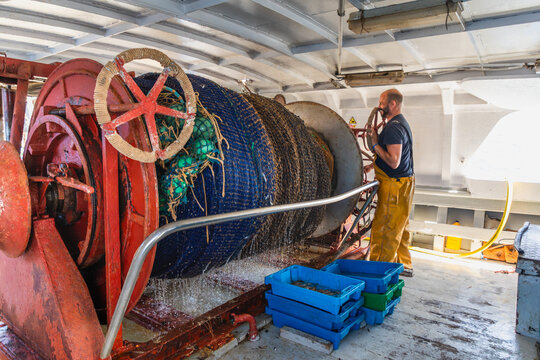 Fisherman hauling trawl net on deck with winch