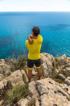 Athlete on rocky trail by the sea stretching arms