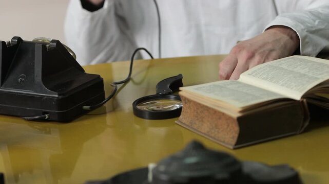 vintage telephone, researcher archive, archivist reading. Close-up researcher or archivist reading antique book while speaking on vintage telephone, with magnifying glass and historical optical device