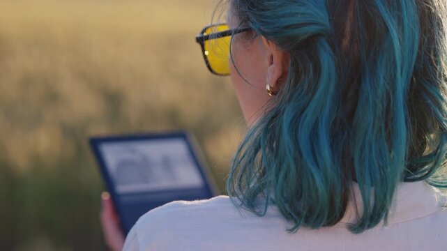 Woman reading with e-reader - electronic book in warm evening sunlight. Portable technology, digital learning, leisure reading and modern lifestyle.