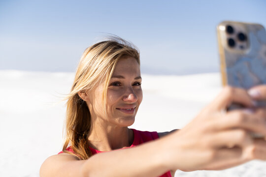 Woman in red dress taking smartphone selfie on white sand