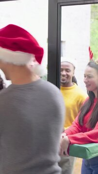Vertical video: Opening front door, host greeting group with antlers and Santa hats, bringing gifts