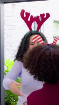 Vertical video: Magenta host hugging guests in home entry after door opening for holiday with gifts