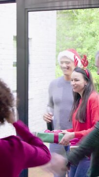 Vertical video: Door opening group wearing antlers greeting passing gifts at glass door for holiday