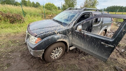 Black pickup truck stuck in deep mud on a countryside road with driver side door open and winch cable pulled. © AndreyZayats