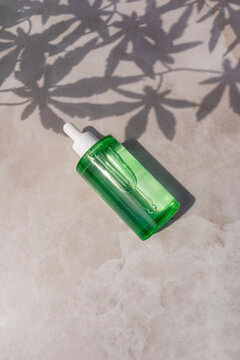 Green skincare serum bottle with leaf shadow on stone