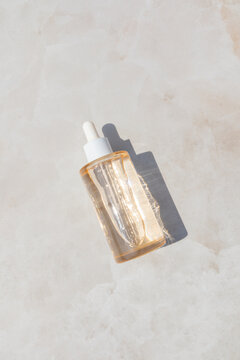 Skincare serum dropper bottle on sunlit neutral surface
