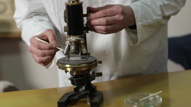 laboratory scientist, microscope slide, antique microscope. Close-up scientist using fine laboratory instrument to prepare microscope slide with antique microscope.