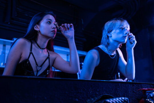 Actors apply makeup backstage under blue stage lighting
