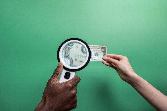 Multiethnic hands inspecting US dollar with magnifier