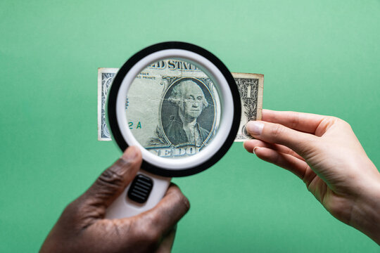 Multiethnic hands inspect a US dollar bill with magnifier