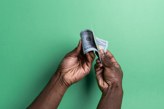 Hands of black man counting US dollar bills on green background