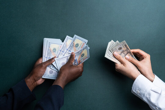 Multiethnic hands counting US dollar cash on dark table
